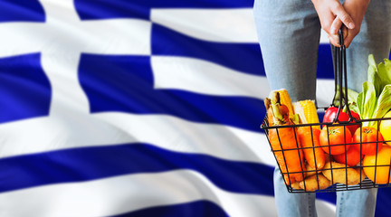 Woman is holding supermarket basket, Greece waving flag background. Economy concept for fresh...