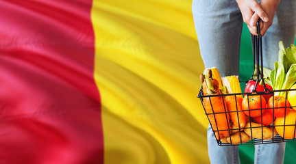 Woman is holding supermarket basket, Guinea waving flag background. Economy concept for fresh fruits and vegetables.