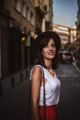 beautiful young woman looking at the horizon at dusk in one of the streets of the city of Madrid with hat, handbag and other accessories. Visit the city at sunset. Travel concept.