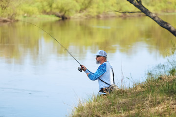 Man fish with spinning on river bank, casting lure. Outdoor weekend activity. Photo with shallow depth of field taken at wide open aperture.