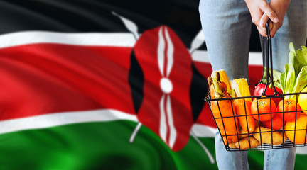 Woman is holding supermarket basket, Kenya waving flag background. Economy concept for fresh fruits and vegetables.
