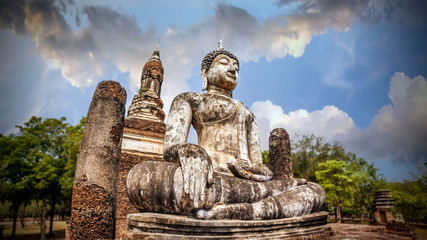 Fototapeta na wymiar Meditating Buddha on the background of the temple and beautiful sky. Wat Traphang Ngoen at Sukhothai Historical Park, a UNESCO World Heritage Site in Thailand