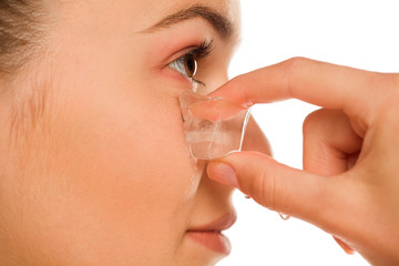 Portrait of young beautiful holding ice cube under her eye on white background