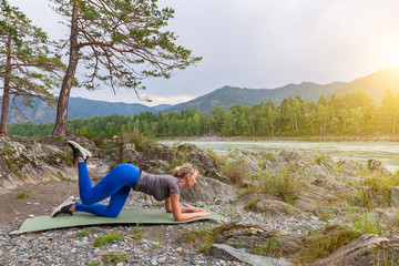 Slim young healthy sports girl doing the donkey kick exercise on all fours arching back straightening leg up concept sport, fitness, lifestyle. Work out and warm up outdoors in mountains near river.