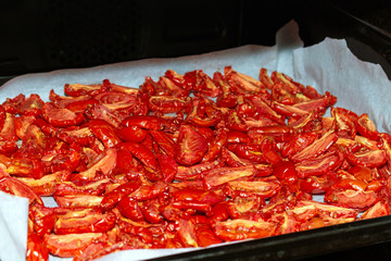 Homemade dried red  tomatoes slices with basil oregano spices cooking process. Traditional Italian Mediterranean kitchen cuisine.