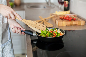 Girl cooks vegetables on the stove, stirring with a wooden shovel.