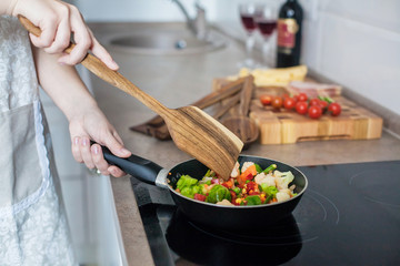 Girl cooks vegetables on the stove, stirring with a wooden shovel.