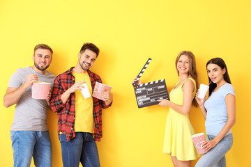 Friends with popcorn and movie clapper on color background