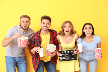 Emotional friends with popcorn and movie clapper on color background