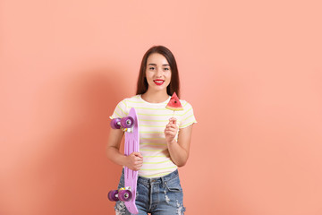 Beautiful young woman with slice of fresh watermelon and skateboard on color background