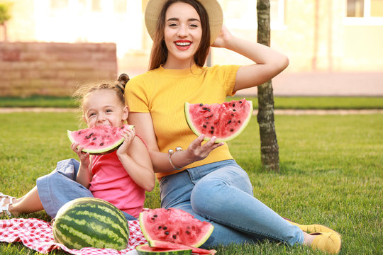 Cute little girl and her mother eating sweet watermelon in park - Powered by Adobe