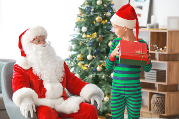 Santa Claus and little elf kid with gift in room decorated for Christmas