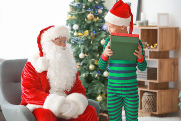 Santa Claus and little elf kid with gift in room decorated for Christmas