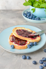 Plate with tasty toasted bread and blueberry jam on grey table