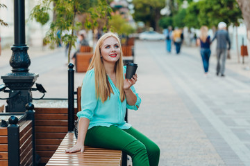 Portrait happy smile beautiful elegant woman blue blouse sitting on a bench and holding a paper cup of coffee