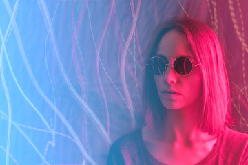 Girl in neon light on dark background, dressed in green glasses.