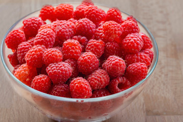 ripe red raspberries in a glass bowl on a wooden background as a natural background.