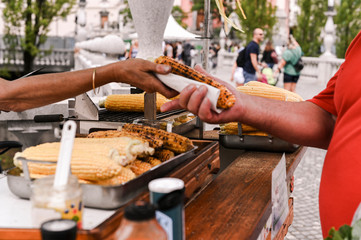 Grilled corn. Fast food in the city center for tourists. Selling food on the street. Hands in the frame of the buyer and seller.