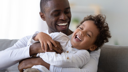 Happy black father tickling african kid son laughing cuddling together