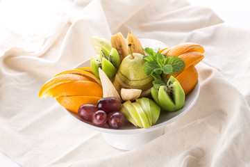 Raw fruits assortment platter with orange, pear, grape and kiwi on white crumpled tablecloth