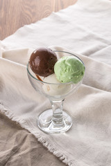 three scoops of chocolate, pistachio and vanilla ice cream in glass bowl on white napkin