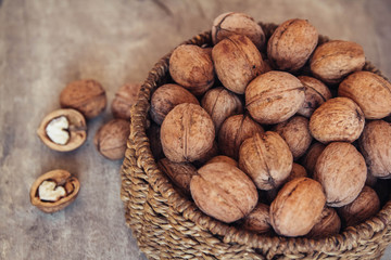 Walnuts in a round wicker basket on a wooden background. Top view. Copy, empty space for text