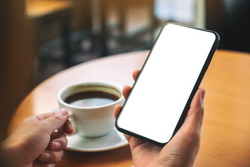 Mockup image of hands holding black mobile phone with blank desktop screen while drinking coffee