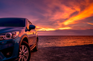 Blue compact SUV car with sport and modern design parked by beach at sunset. Hybrid and electric car technology. Car parking space. Automotive industry. Car care business background. Beautiful sky.
