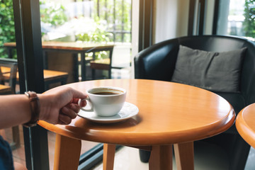 Closeup image of a hand holding a cup of hot coffee on table