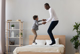 Happy black father and cute kid son jumping on bed