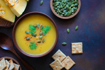 Roasted butternut squash cream soup with pumpkin seeds,pumpkin slices on dark background,copy space,top view