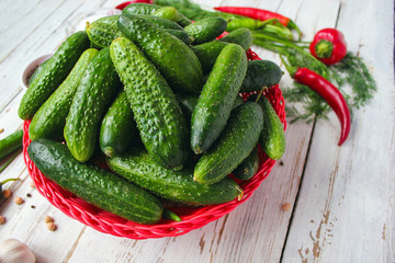 Fresh organic cucumbers in red basket  on white wooden table with green and red and chilli peppers,fennel,salt,black peppercorns,garlic,pea,close up,healthy concept,top view,flat lay