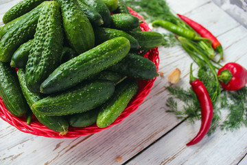 Fresh organic cucumbers in red basket  on white wooden table with green and red and chilli peppers,fennel,salt,black peppercorns,garlic,pea,close up,healthy concept,top view,flat lay