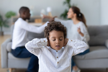 Upset african kid son closing ears not listening parents fighting