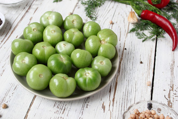 green tomatoes,pickles background on white wooden table with green and red and chilli peppers,fennel,salt,black peppercorns,garlic,pea,close up,healthy concept,top view,flat lay