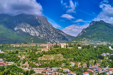 Obraz premium The resort town of Pulciano, located on the shores of Lake Garda. San Michele Arcangelo Church is located on a mountain. Panoramic view of the city, church, Lake Garda, Alps. Aerial view.