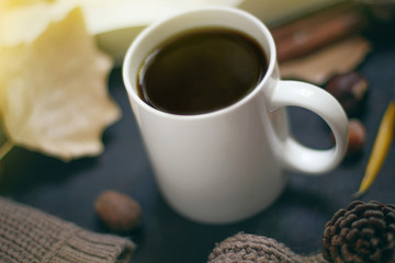 Autumn, fall leaves, hot steaming cup of coffee and a warm scarf or cardigan on black old background. Seasonal, morning coffee, Sunday relaxing and still life concept.Space for copy