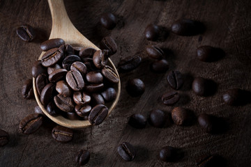 coffee beans on wooden spoon on the brown wood table.