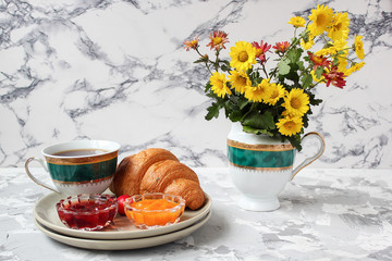 French breakfast with croissants,apricot jam,cherry jam and a cup of tea,red and yellow flowers on white concrete background,close up,space for text,Valentine`s Day breakfast