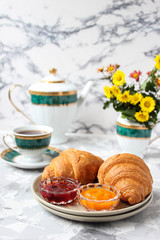 French breakfast with croissants,apricot jam,cherry jam and a cup of tea,red and yellow flowers on white concrete background,close up,space for text,Valentine`s Day breakfast