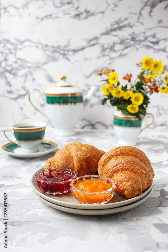 Wall mural French breakfast with croissants,apricot jam,cherry jam and a cup of tea,red and yellow flowers on white concrete background,close up,space for text,Valentine`s Day breakfast