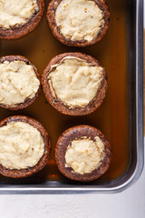Baked stuffed champignon caps and baked cherry tomatoes on baking sheet. Mushrooms stuffed with vegan cashew mayonnaise.  Vegetarian food concept. Top view. Close-up.