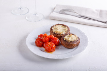 Baked stuffed champignon caps and baked cherry tomatoes on white plate. Mushrooms stuffed with vegan cashew mayonnaise. Vegetarian food concept.