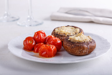 Baked stuffed champignon caps and baked cherry tomatoes on white plate. Mushrooms stuffed with vegan cashew mayonnaise. Vegetarian food concept.
