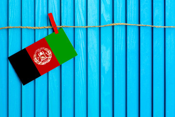 Flag of Afghanistan hanging on clothesline attached with wooden clothespins on aqua blue wooden background. National day concept.