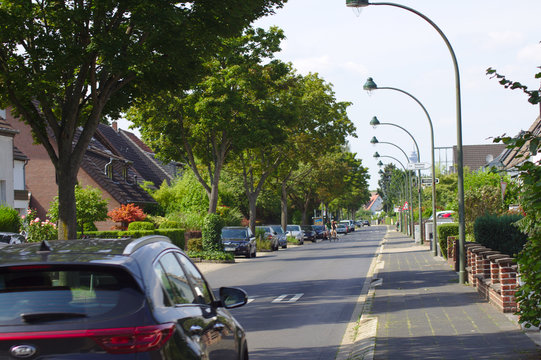 Eine Strasse mit fahrendem Auto und Strassenlaternen im Wohngebiet, parkende Autos und Häuser