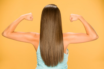 Back view of young woman with long hair, showing her hands on yellow background