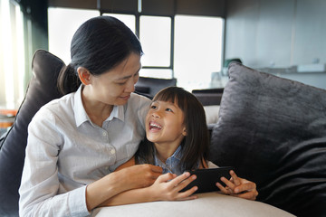 Asian mother and daughter watching cartoon on smartphone happily in the living room, quality time concept