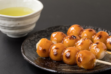 黒い背景にタレがたっぷりついたみたらし団子とお茶日本のデザート和菓子