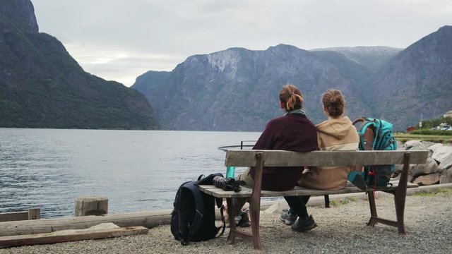 Two young women travelers sitting on the bench with a view to the fjord and resting